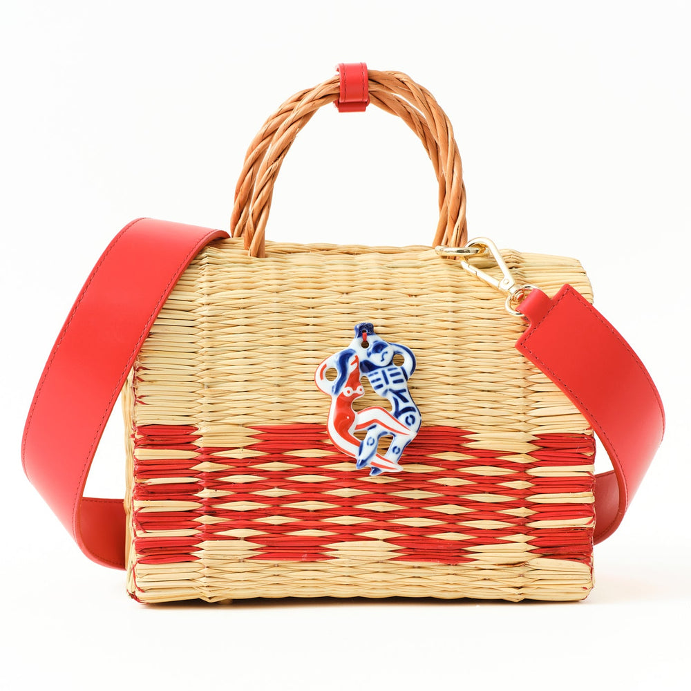 Wicker handbag with red accents and a decorative emblem on a white background
