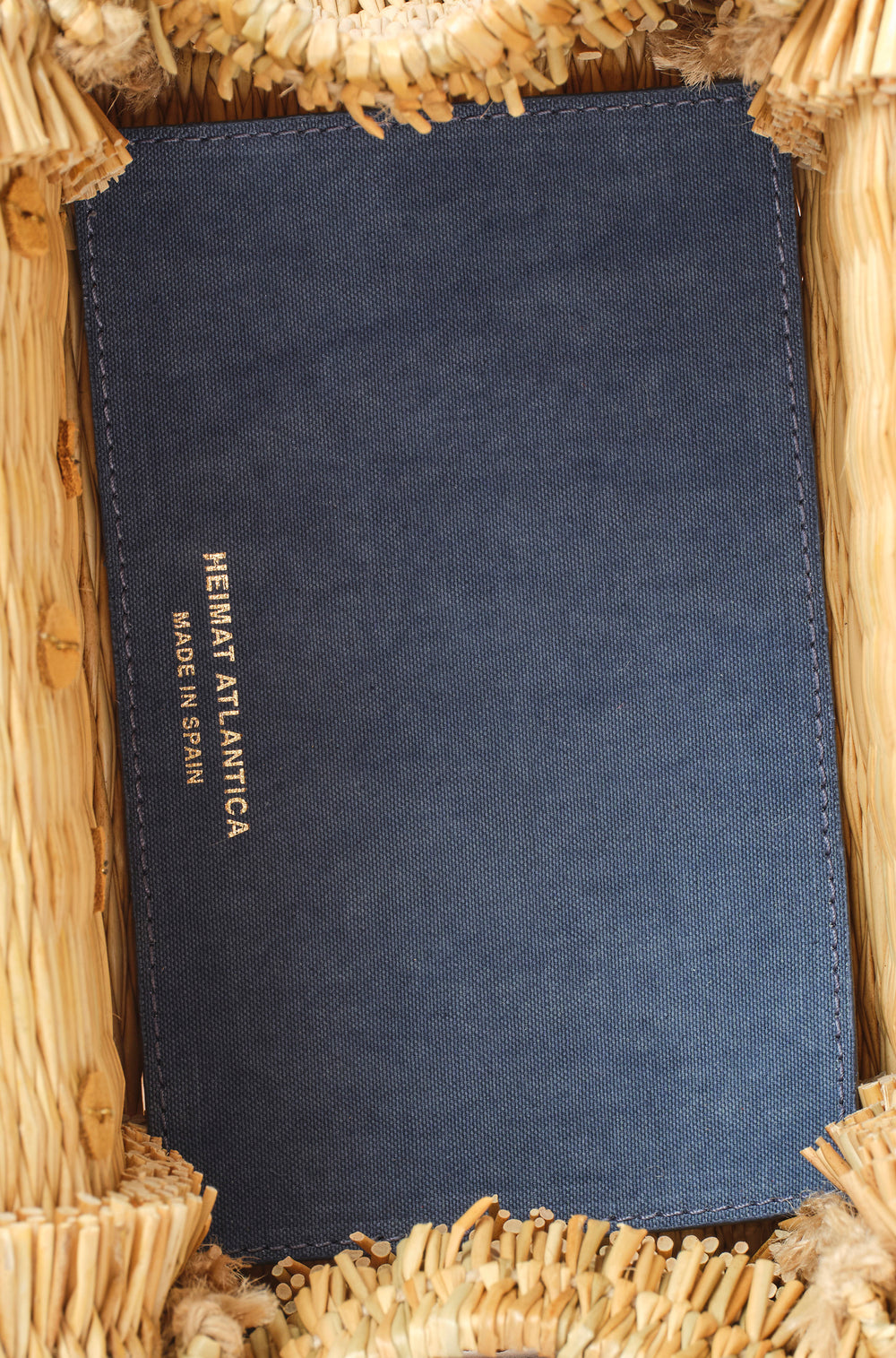 Shella Denim Classic basket bag by Heimat Atlantica, woven in Portugal from reed and finished in Spain with an Atlantic shell charm. Interior detail with branding. 