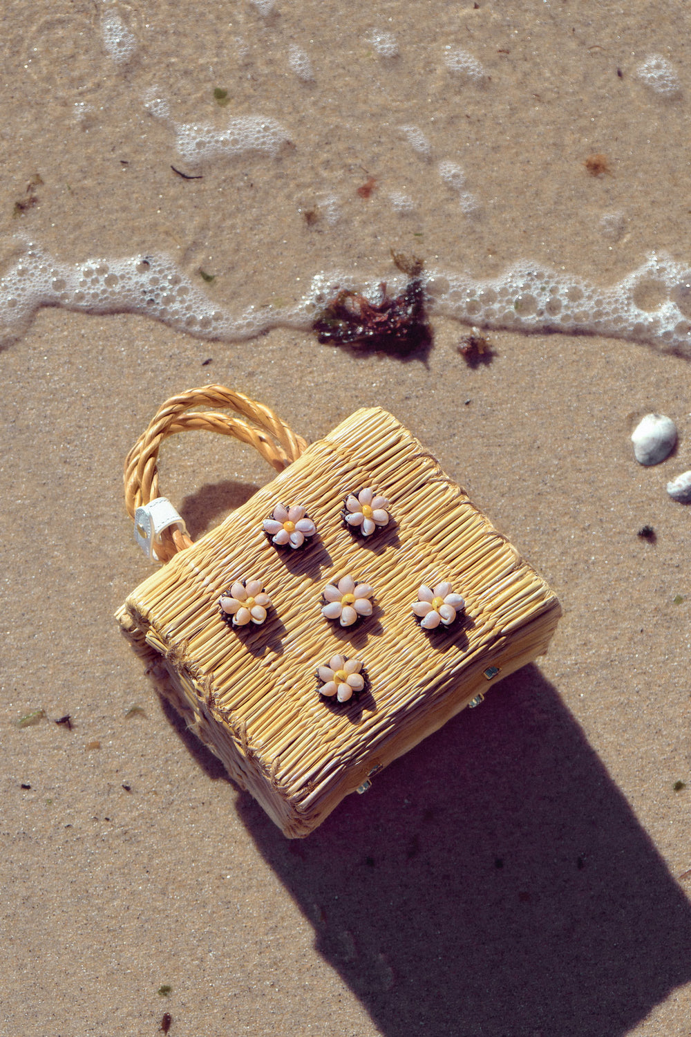 Shella Mini White basket bag by Heimat Atlantica, handwoven in Portugal from natural reed and finished in Spain with an Atlantic shell details. View in the beach. 