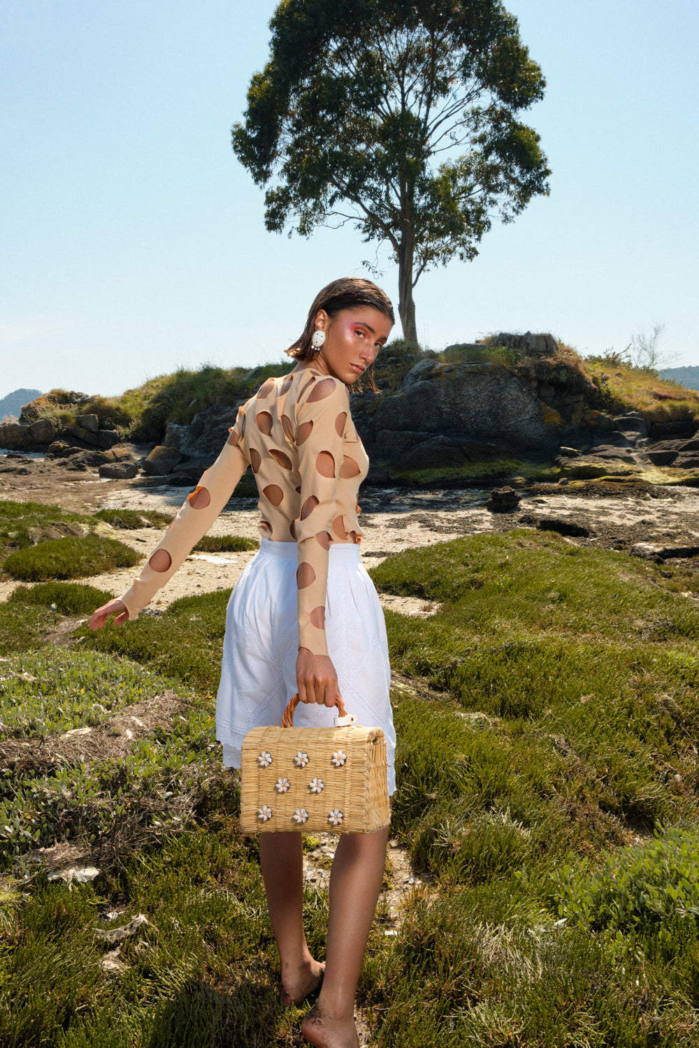 Model wearing the Shella Medium White bag and wearing Lares earrings by Heimat Atlantica, standing by the Atlantic shore.