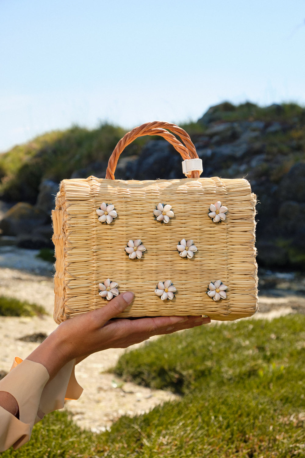Model holding the Shella Medium White bag and wearing Lares earrings by Heimat Atlantica, with the Atlantic coast in the background.